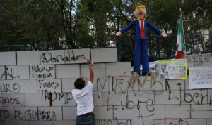 A demonstrator writes on symbolic wall as is seen a pinata representing the U.S. President Donald Trump during a protest outside the U.S. embassy, in Mexico City, Mexico January 20, 2017. REUTERS/Edgard Garrido - RTSWLX4